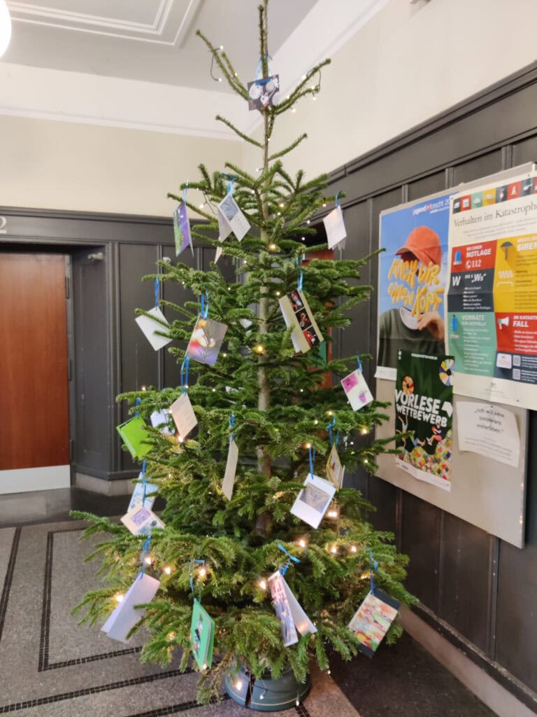 Ein Weihnachtsbaum mit Karten, Lichtern und einem Wandplakat im Hintergrund.