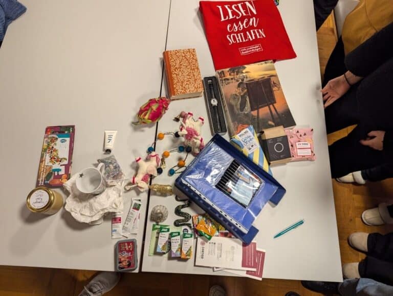 Verschiedene Gegenstände auf Tisch; bunte Dekorationen, Bücher, ein rotes T-Shirt.