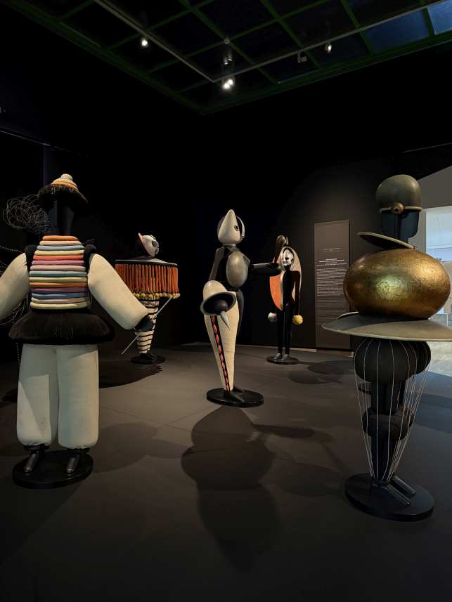 Fünf farbenfrohe, abstrakte Figuren in einem Museumsraum mit dunkler Beleuchtung.