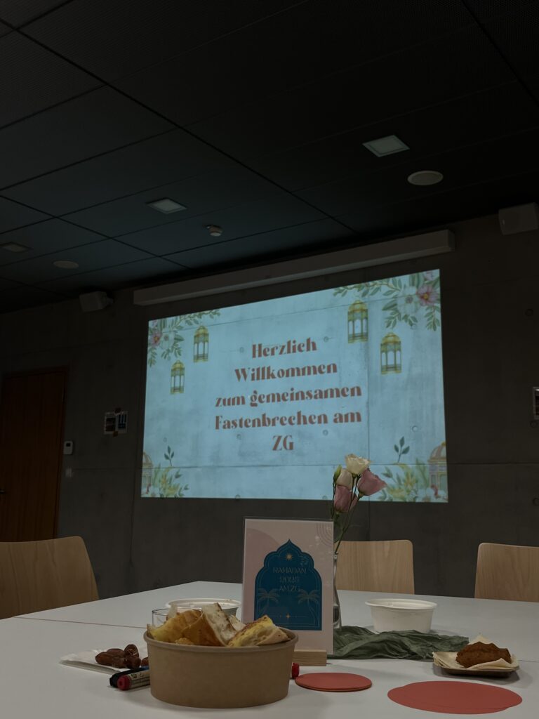 Projektion mit Text "Herzlich Willkommen", dekorativer Tisch mit Snacks und Blumen, moderner Raum.