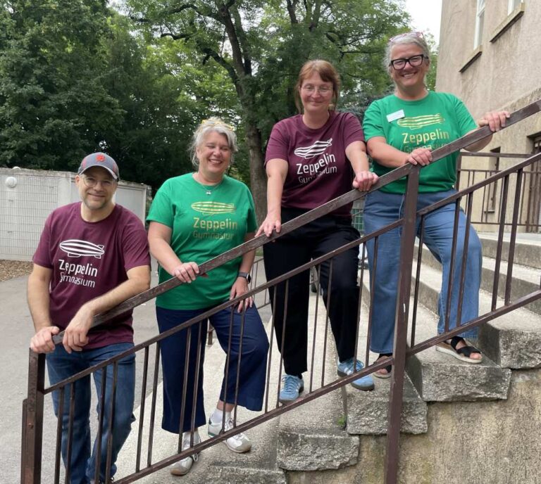 Vier fröhliche Personen auf einer Treppe tragen bunte T-Shirts.