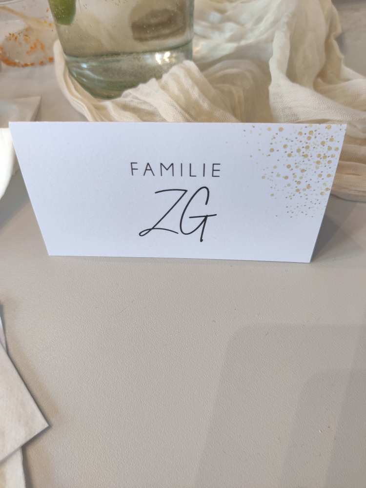 Tischkarte mit der Aufschrift "FAMILIE ZG", dekoriert mit goldenen Punkten, auf beige Stoff.
