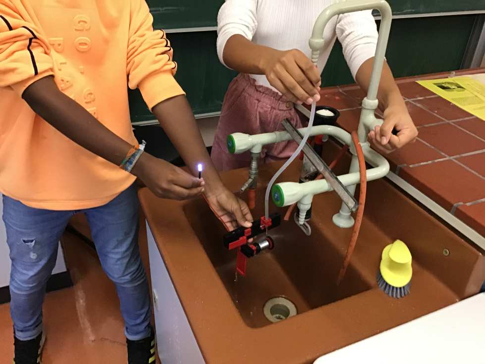 Zwei Personen experimentieren an einem Schulwaschbecken mit einem Laborsetup und Schläuchen.