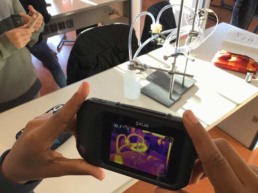 Eine Person hält ein Infrarotgerät in einem Labor mit Apparatur im Hintergrund.