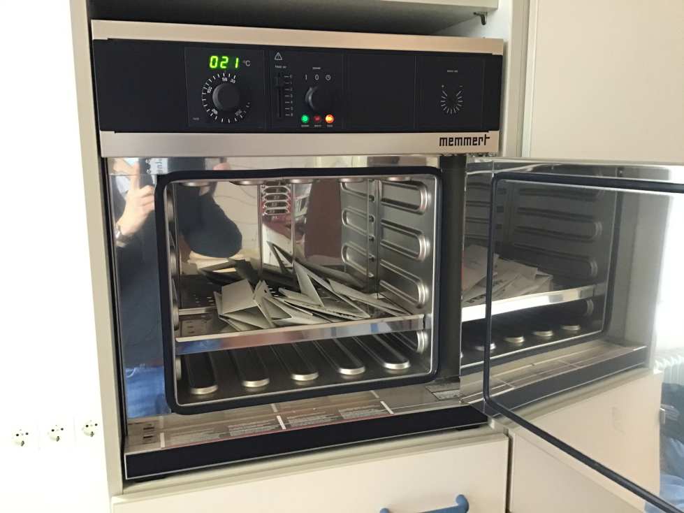 Ein geöffneter Memmert-Ofen mit Papieren im Inneren, Temperaturanzeige zeigt 21 Grad Celsius.