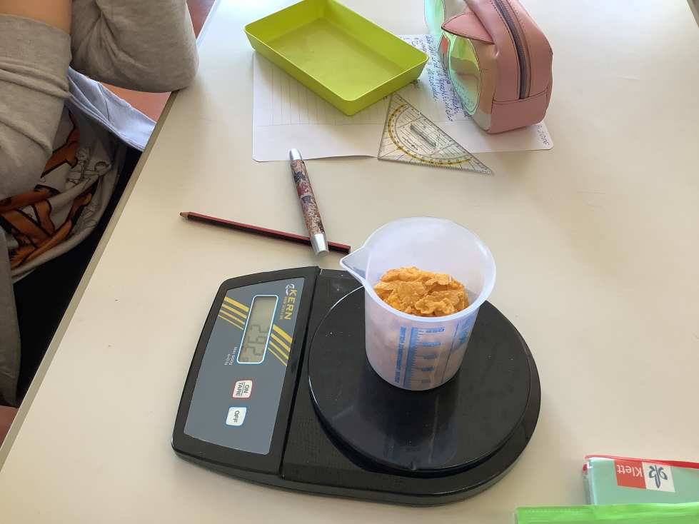 Eine Person wiegt Cornflakes auf einer digitalen Waage im Klassenzimmer.
