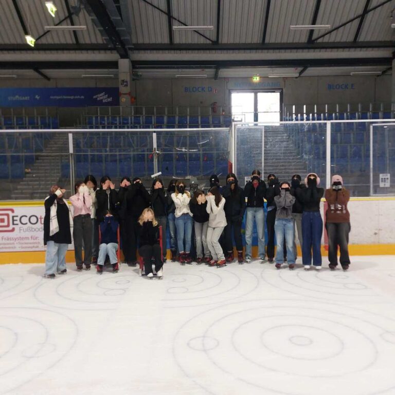 Eine Gruppe Jugendlicher auf einer Eisbahn verdeckt lachend ihre Gesichter vor der Kamera