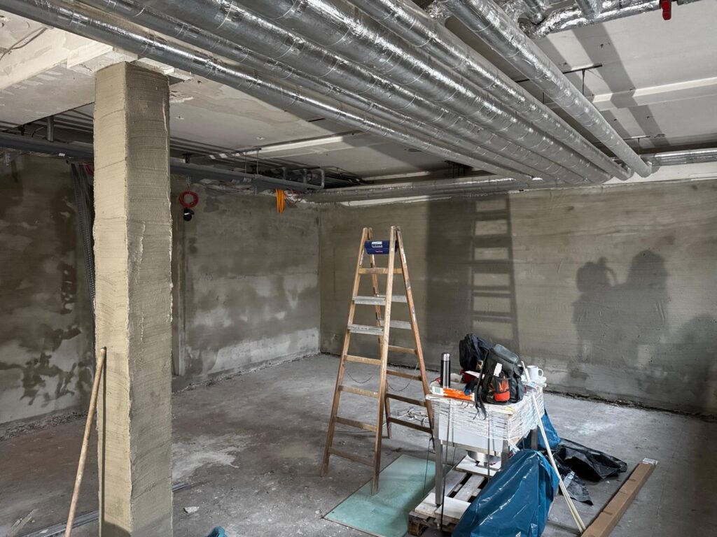 Ein leerer Rohbau mit grauen Wänden, einer Holzleiter und Bauwerkzeugen auf dem Boden