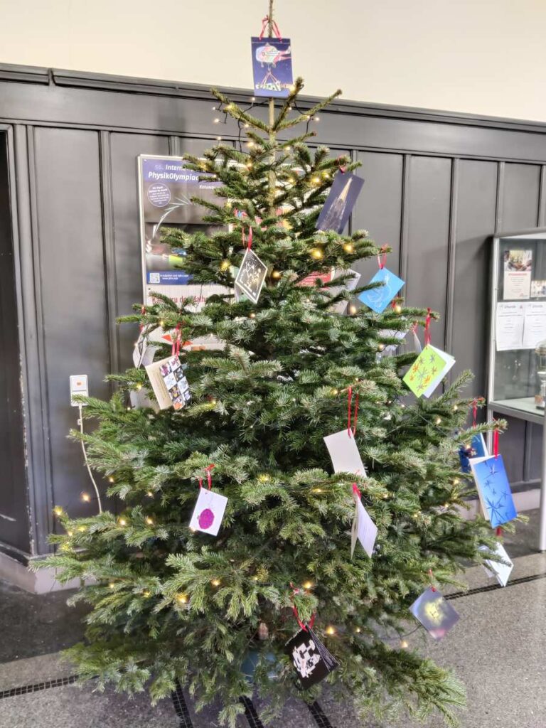 Ein reich geschmückter Weihnachtsbaum steht mit vielen Karten und Lichtern im Raum