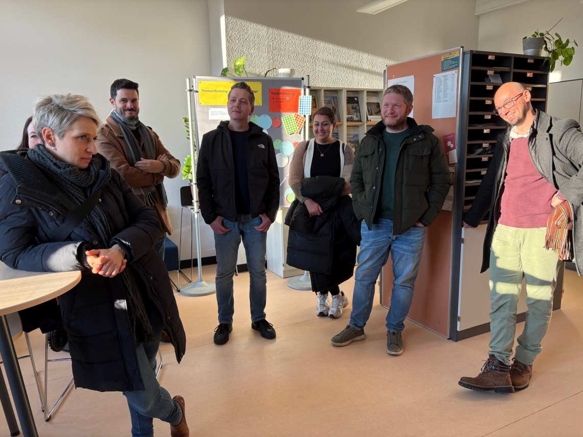 Sechs Erwachsene stehen entspannt und lachend in einem sonnigen Bürobereich