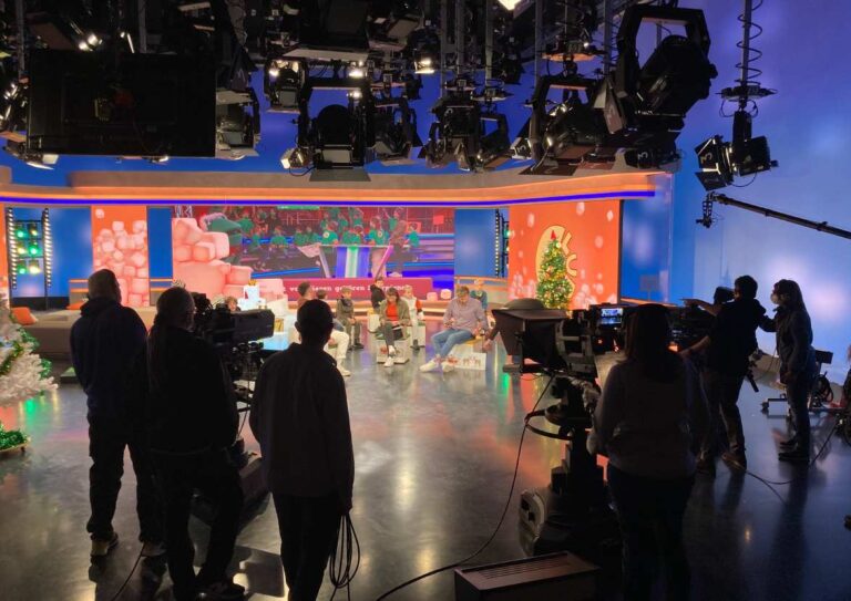 Im Fernsehstudio sitzen mehrere Personen entspannt auf bunten Sesseln vor Weihnachtsdeko