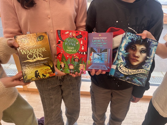 Vier Kinder halten lächelnd bunte Bücher mit verschiedenen Covern in den Händen