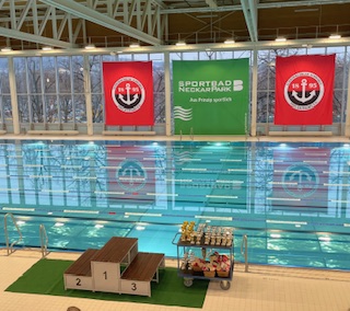 Ein leeres Schwimmbecken mit Startblöcken, Siegerehrungspodest und rotweißen Vereinsbannern