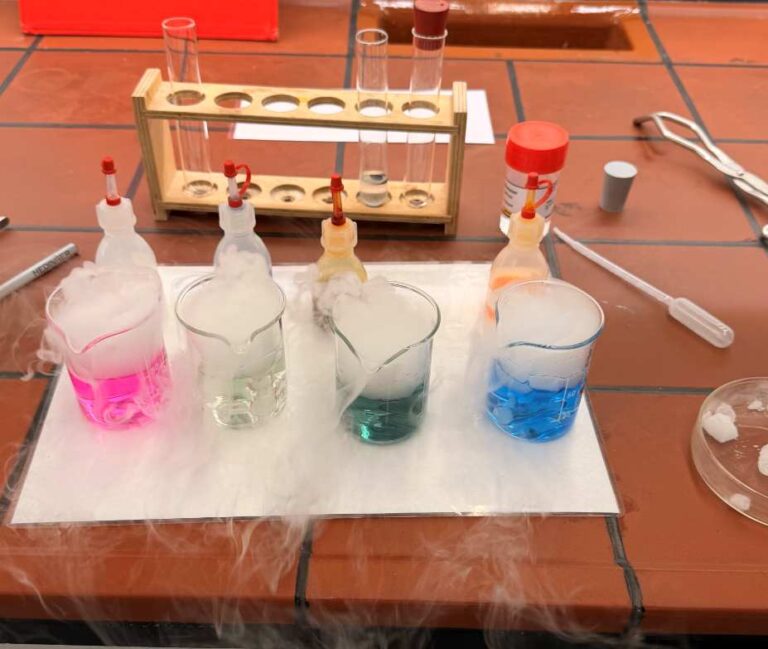 Mehrere Glasbecher mit bunten Flüssigkeiten und Nebel auf einem Labortisch