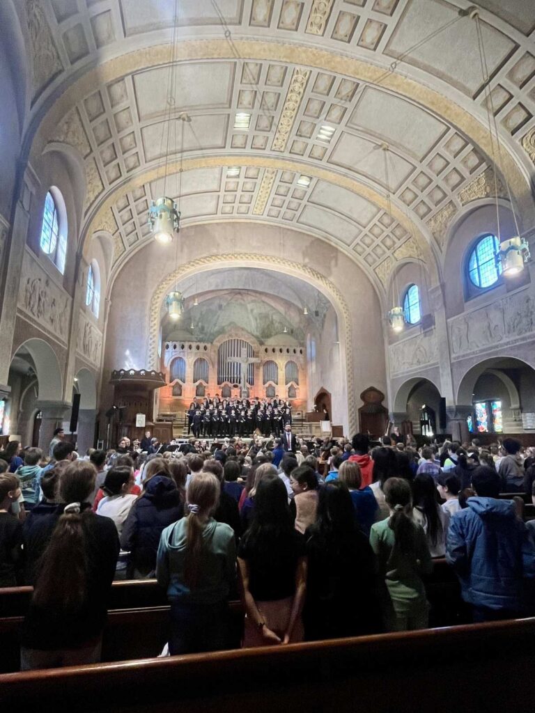 Eine große Gruppe Jugendlicher singt auf einer Kirchenbühne vor aufmerksamem Publikum