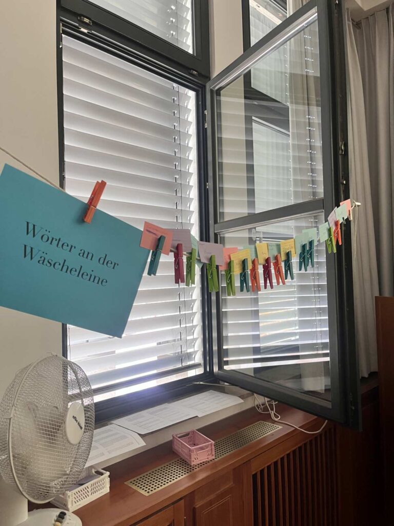 Offenes Fenster mit bunten Wortkarten an Wäscheleine und Ventilator